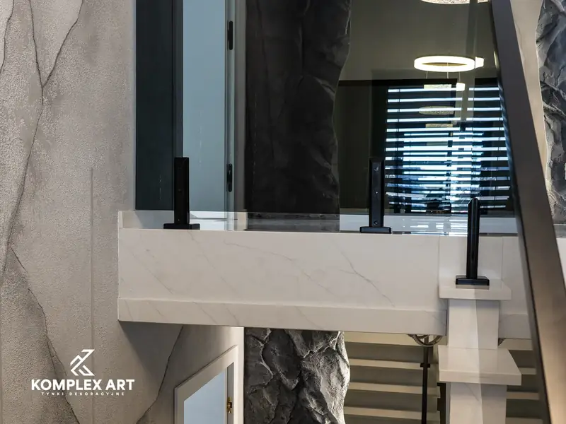 Klatka schodowa ze ścianą w efekcie skały i jasną, marmurową balustradą, realizacja Komplex Art