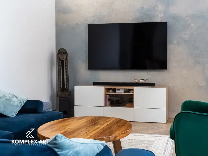 Salon z telewizorem na ścianie w efekcie wabi-sabi, niebieska kanapa i drewniany stolik, realizacja Komplex Art